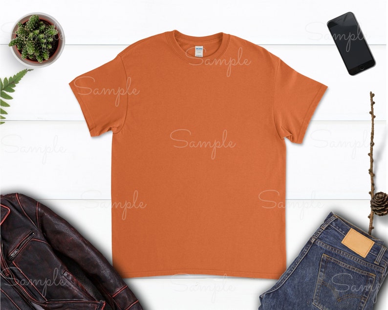 May include: A plain orange t-shirt on a white wood background. The t-shirt is a blank canvas for customization.