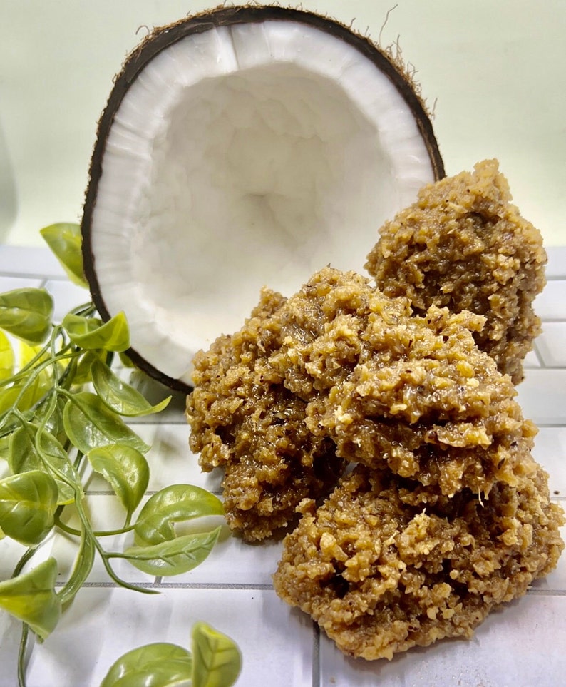 May include: A close-up of a pile of brown coconut candy, with a half of a coconut shell in the background.