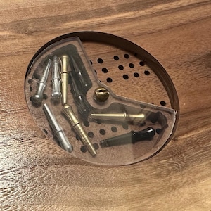 Può includere: Primo piano di un tavolo di legno con un'intarsio circolare. L'intarsio è pieno di una varietà di piccoli strumenti colorati, tra cui argento, oro e nero.