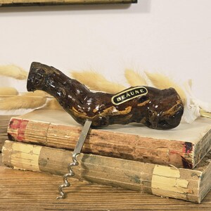 May include: A vintage corkscrew with a dark brown, textured wooden handle and a silver metal corkscrew. The handle has a label that reads "BEAUNE". The corkscrew is resting on top of two antique books.