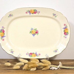 May include: Cream-colored oval serving platter with a scalloped edge and gold trim. The platter is decorated with clusters of colorful flowers in yellow, pink, and purple. A decorative piece for serving food.