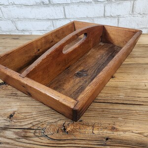 May include: A rustic wooden tray with a built-in handle. The tray is made of natural wood and has a warm brown colour. It has a divided section for organising items.