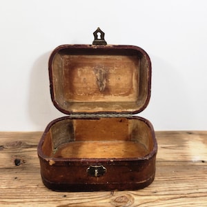 May include: An antique wooden box with a brown leather exterior and a brass latch. The box is open and the inside is empty.