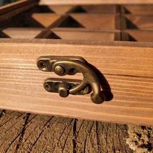 Op de afbeelding: Een houten doos met een scharnierend deksel en een messing sluiting. De doos heeft meerdere compartimenten en is gemaakt van donkerbruin hout.