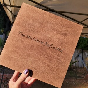 On the bottom the text "The Universe Reflected" written in cursive.