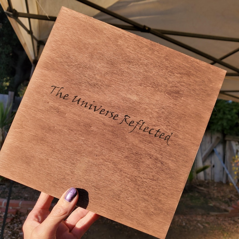 On the bottom the text "The Universe Reflected" written in cursive.
