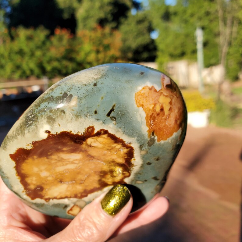 May include: A polished stone with a mix of colors, including teal, brown, and tan. The stone has a smooth, rounded shape and a unique pattern. The colors blend together, creating an interesting and natural look. This stone is a decorative item.