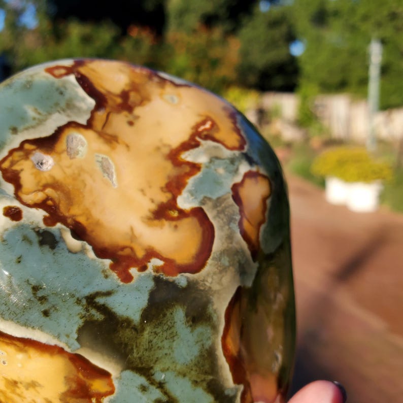 May include: A polished stone with a unique pattern of tan, brown, and teal colors. The stone's surface has a smooth, glossy finish, with the colors blending together in an abstract design. The stone is a natural, decorative item.