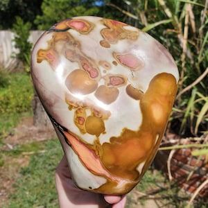 May include: A polished stone with a unique pattern of colors. The stone features a mix of white, brown, orange, and pink hues. The colors blend together in a swirling, organic design. The stone is smooth and has a rounded shape, making it a decorative item.