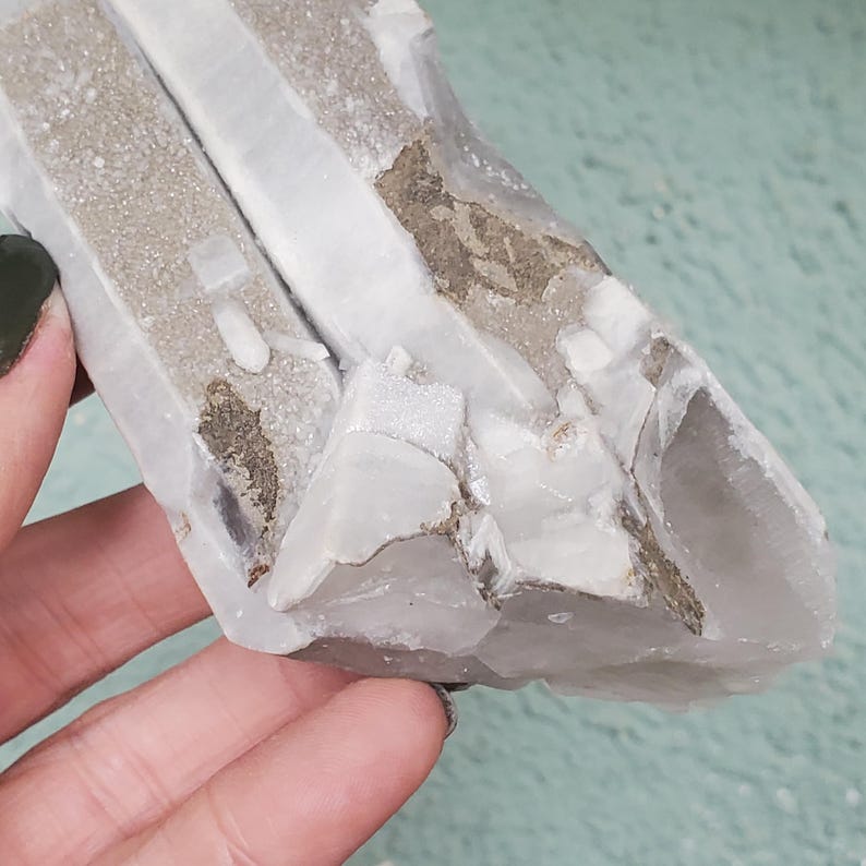 Pu&ograve; includere: Un gruppo di cristalli di quarzo grezzo e naturale. Il cristallo presenta un mix di sezioni bianche chiare e opache, con inclusioni beige e grigie. La consistenza ruvida e la forma irregolare ne evidenziano l'origine naturale. Un esemplare minerale unico.