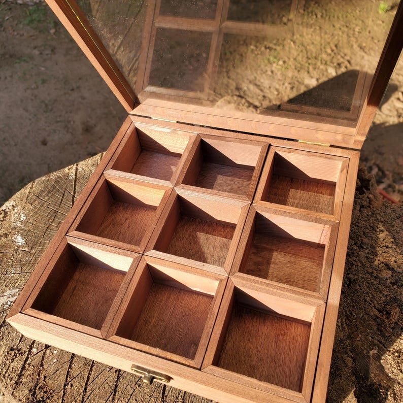 Op de afbeelding: Een houten doos met een glazen deksel en negen vakken. De doos is open en de vakken zijn leeg.