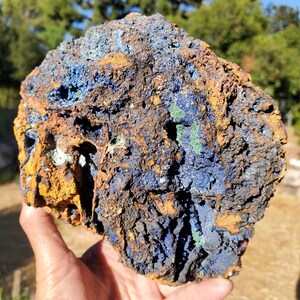 May include: A raw mineral specimen featuring a rough, porous texture with deep blue azurite crystals embedded within a matrix of earthy brown and rust-colored rock, accented by small patches of bright green malachite throughout the surface.