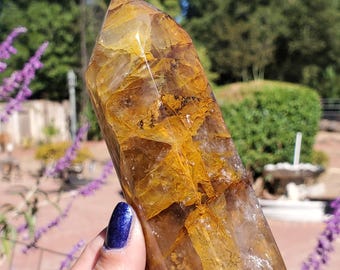 May include: A polished, hexagonal crystal point featuring a translucent golden-yellow and amber color palette with internal fractures, inclusions, and clear crystalline sections throughout the structure of the stone.