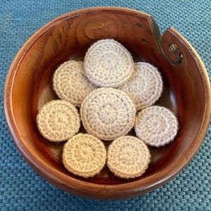 Könnte beinhalten: Eine Holzschale gefüllt mit beigefarbenen gehäkelten Kreisen. Die Schale hat eine dunkelbraune Holzmaserung und einen Griff an der Seite.