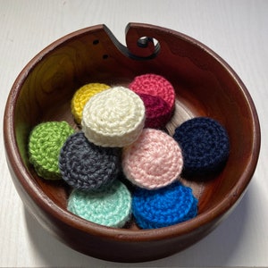 Puede incluir: Un cuenco de madera lleno de nueve posavasos de ganchillo en varios colores, incluyendo verde, blanco, rosa, azul, amarillo y rojo.