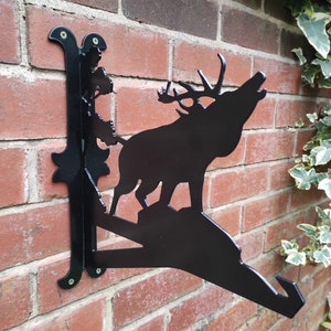 May include: Black metal wall bracket featuring a silhouette of a stag with antlers, standing on a rocky base. The bracket is attached to a brick wall with screws.