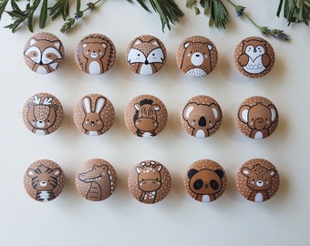 May include: A collection of fifteen wooden cabinet knobs, each featuring a different hand-painted animal design. The knobs are brown with white polka dots and the animals include a raccoon, hedgehog, fox, bear, owl, deer, rabbit, zebra, koala, elephant, tiger, alligator, giraffe, panda, and leopard.