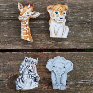Può includere: Quattro figurine di animali in legno, dipinte con dettagli realistici. Una girafe con macchie marroni e arancioni, un cucciolo di leone con un mantello marrone chiaro e bianco, una zebra con strisce nere e bianche e un elefante con la pelle grigia.