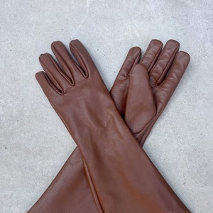 Peut inclure: Une paire de longs gants en cuir marron à la coupe simple. Les gants sont croisés l'un sur l'autre.