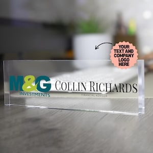 May include: A clear acrylic desk nameplate with the text "M&G INVESTMENTS" in teal and lime green, and "COLLIN RICHARDS FINANCIAL ADVISOR" in black. A pink sticker indicates where to add a logo.