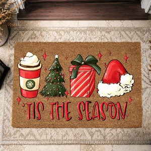 Op de afbeelding: Een rechthoekige bruine kokosmat met een rode koffiebeker met slagroom, een groene kerstboom, een rood cadeau met een groene strik en een rode kerstmuts. De tekst 'TIS THE SEASON' staat in rode letters onder de illustraties afgebeeld.