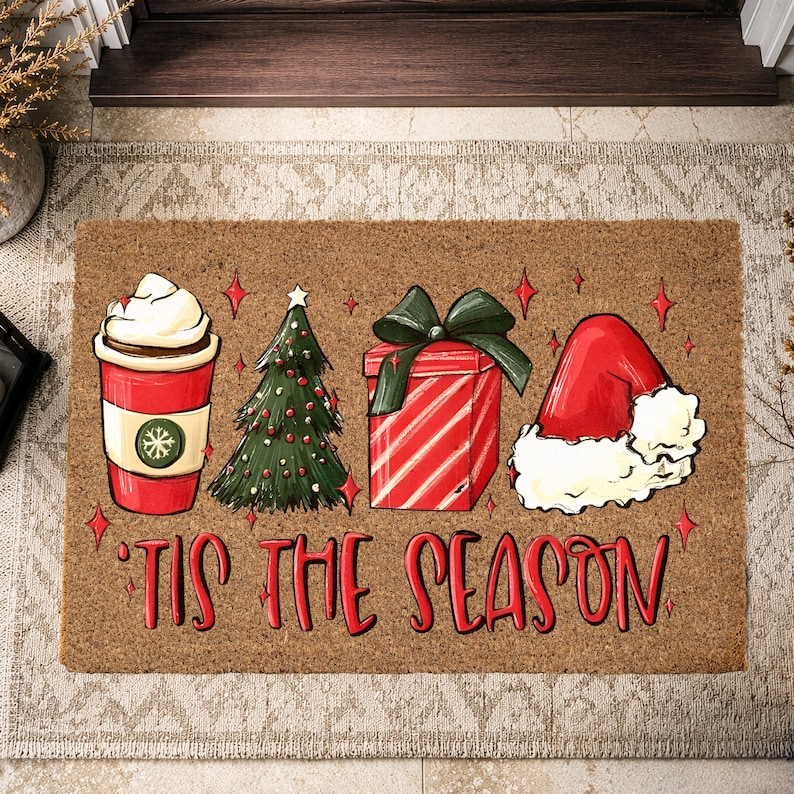 Op de afbeelding: Een rechthoekige bruine kokosmat met een rode koffiebeker met slagroom, een groene kerstboom, een rood cadeau met een groene strik en een rode kerstmuts. De tekst 'TIS THE SEASON' staat in rode letters onder de illustraties afgebeeld.