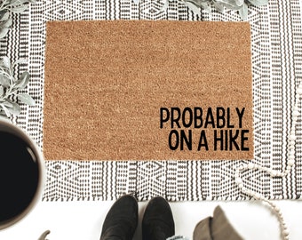 May include: A brown doormat with the text "Probably on a hike" in black lettering.