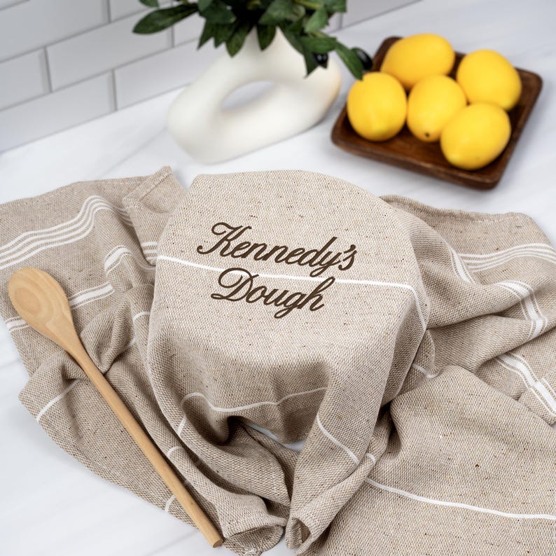 personalized sourdough dough cover with custom name on neutral cloth draped over bread bowl with wooden spoon and lemons in kitchen