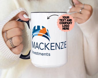 May include: A white ceramic mug with a dark blue handle and interior. The front features a blue and orange geometric logo above the text MACKENZIE Investments. A pink circular graphic with the text YOUR TEXT AND COMPANY LOGO HERE is included.