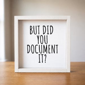 Close-up of the white-framed office humor sign, showing “But Did You Document It?” in tall black lettering on a light background.