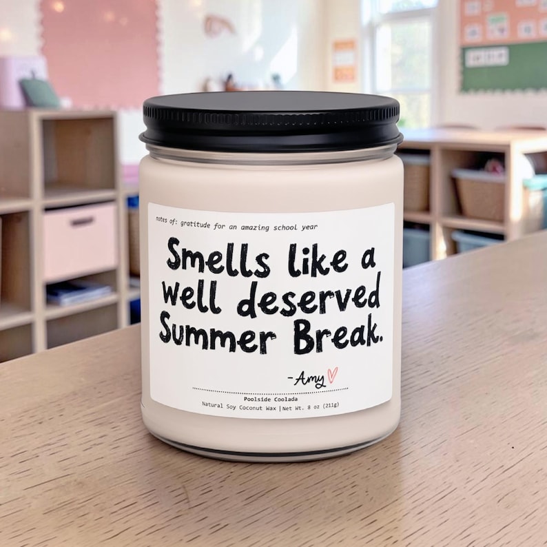 May include: A cream-colored candle in a glass jar with a black lid. The label reads "Smells like a well deserved Summer Break." The candle is labeled "Poolside Coolada" and contains 8 oz (227g) of natural soy coconut wax.
