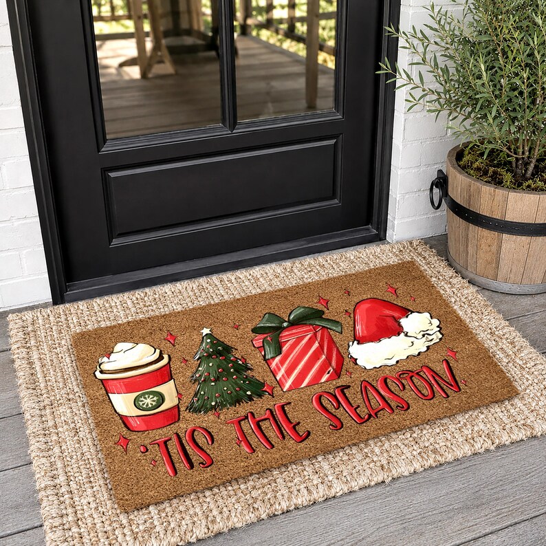 Op de afbeelding: Een rechthoekige bruine kokosmat met een rode koffiebeker, een groene kerstboom, een rood cadeau met een groene strik en een rode kerstmuts. De tekst 'TIS THE SEASON' staat in rode letters onderaan de deurmat afgebeeld.