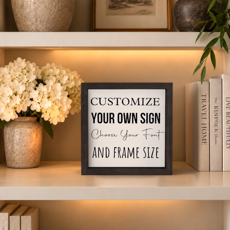 Black-framed custom quote sign displayed on a softly lit bookshelf between flowers and books, with black sample lettering on a white background.