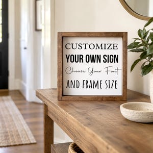Brown-framed custom wording sign on an entryway console beside a ceramic bowl and leafy plant, with a front door in the background.