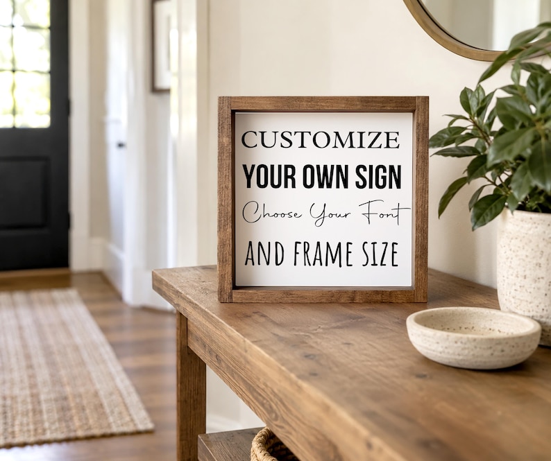 Brown-framed custom wording sign on an entryway console beside a ceramic bowl and leafy plant, with a front door in the background.