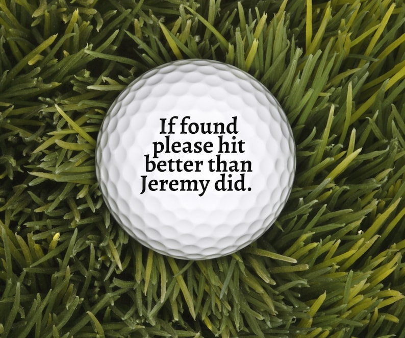 May include: A white golf ball with a dimpled surface featuring the black printed text: If found please hit better than Jeremy did. The ball is spherical and displays a standard professional design with clear, legible lettering centred on the front.