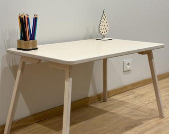 May include: A white wooden table with a light wood finish. The table has four legs and a rectangular top. There is a pencil holder with coloured pencils on the table, and a small wooden Christmas tree decoration.