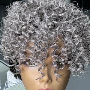 May include: A gray curly hair topper with a side part. The hair topper is made of synthetic hair and is designed to add volume and length to your hair.