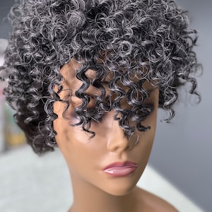 Puede incluir: Una peluca corta y rizada con cabello negro y gris. La peluca está peinada con raya lateral y el cabello está rizado en un patrón de espiral apretado.