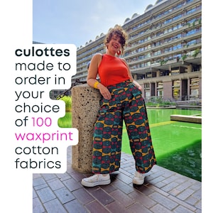 May include: Culottes featuring a geometric wax print pattern in teal, yellow, and red, paired with a sleeveless orange top and white sneakers. Text on the image reads: culottes made to order in your choice of 100 waxprint cotton fabrics.
