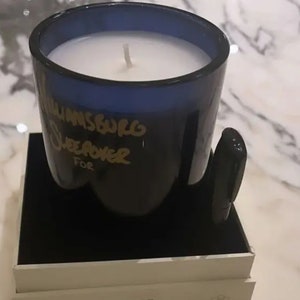K&ouml;nnte beinhalten: Ein blaues Glasgef&auml;&szlig; mit einer wei&szlig;en Kerze darin. Das Gef&auml;&szlig; tr&auml;gt eine goldene Aufschrift "Williamsburg Sweet Power For". Die Kerze steht auf einer schwarzen Box mit dem Aufdruck "BW PH BETTER WORLD FRAGRANCE / HOUSE" auf der Seite.