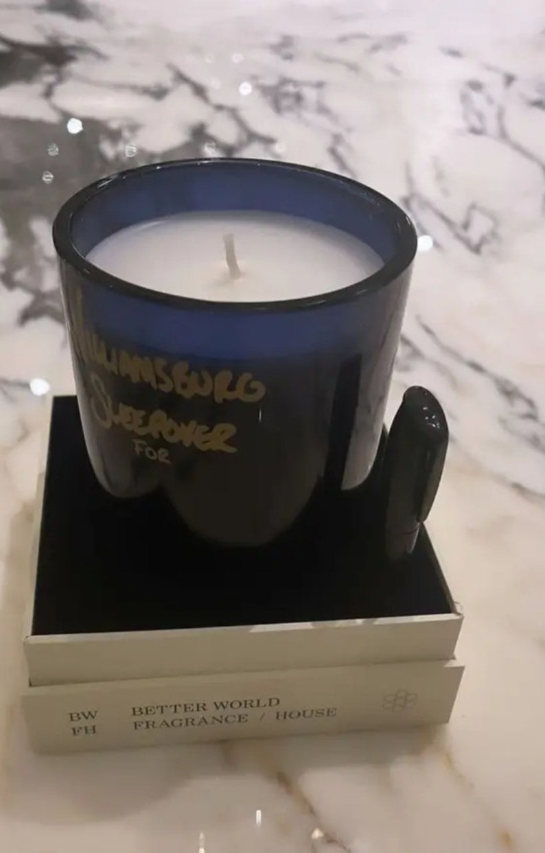 K&ouml;nnte beinhalten: Ein blaues Glasgef&auml;&szlig; mit einer wei&szlig;en Kerze darin. Das Gef&auml;&szlig; tr&auml;gt eine goldene Aufschrift "Williamsburg Sweet Power For". Die Kerze steht auf einer schwarzen Box mit dem Aufdruck "BW PH BETTER WORLD FRAGRANCE / HOUSE" auf der Seite.