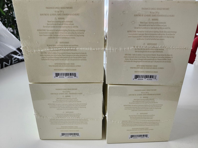 K&ouml;nnte beinhalten: Vier wei&szlig;e Boxen mit schwarzem Text und Barcodes. Die Boxen sind mit "Fragrance Candle, Bougie Parfum&eacute;e, Duftkerze, Vela Aromatica" beschriftet. Der Text auf den Boxen enth&auml;lt Informationen &uuml;ber die Kerze, wie z. B. die Brenndauer, den Duft und das Gewicht. Die Boxen sind &uuml;bereinander gestapelt.