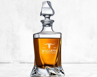 Puede incluir: Una decantador de vidrio transparente con un diseño texturizado y un tapón. El decantador está lleno de líquido ámbar y tiene un diseño grabado en blanco que dice "ESTD 1984 WILLIAMS BEST SCOTCH DRINKER" con un gráfico de cabeza de toro.