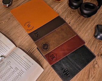 May include: Five leather desk mats in different colors and textures, each with a personalized monogram. The monograms are in a variety of styles, including a wreath, a circle, a hexagon, and a diamond. The mats are arranged in a stack, with the top mat being orange.
