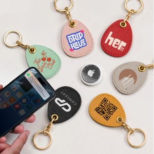 May include: A collection of keychains in various colors, each with a unique design or text. Keychains include a pink one with "DRIP HAUS", a red one with "her", and a black one with "CONCEPT". Also included is an Apple AirTag.