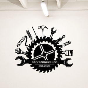 May include: Black and white silhouette of a saw blade with various tools arranged around it. The saw blade has the text "DAD'S WORKSHOP EST. 2023" on it.
