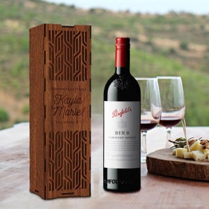 Peut inclure: Une boîte à vin en bois avec un motif géométrique et le texte "Congratulations Kayla Marie! You made it!" Une bouteille de vin Penfolds Bin 8 Cabernet Shiraz est à côté de la boîte.