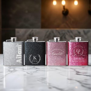 May include: Four silver glitter hip flasks with personalised engravings. The flasks are in silver, black, pink, and red. The engravings include names, initials, and dates.