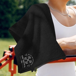 May include: Black cotton towel with a white logo that says "The Smith's Club" with a dumbbell graphic and the text "Est'd 2023 Be Fit Be Stronger".